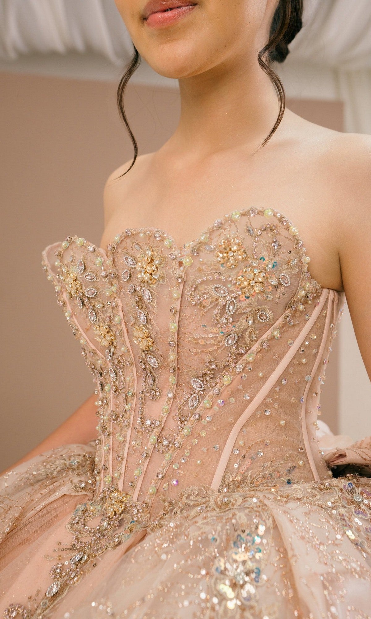 A woman wearing the Quinceanera Dress 8590JQ By Cinderella Couture, a blush ball gown with a strapless beaded corset bodice, ornate embroidery, sequin embellishments, and a flowing glitter tulle skirt.
